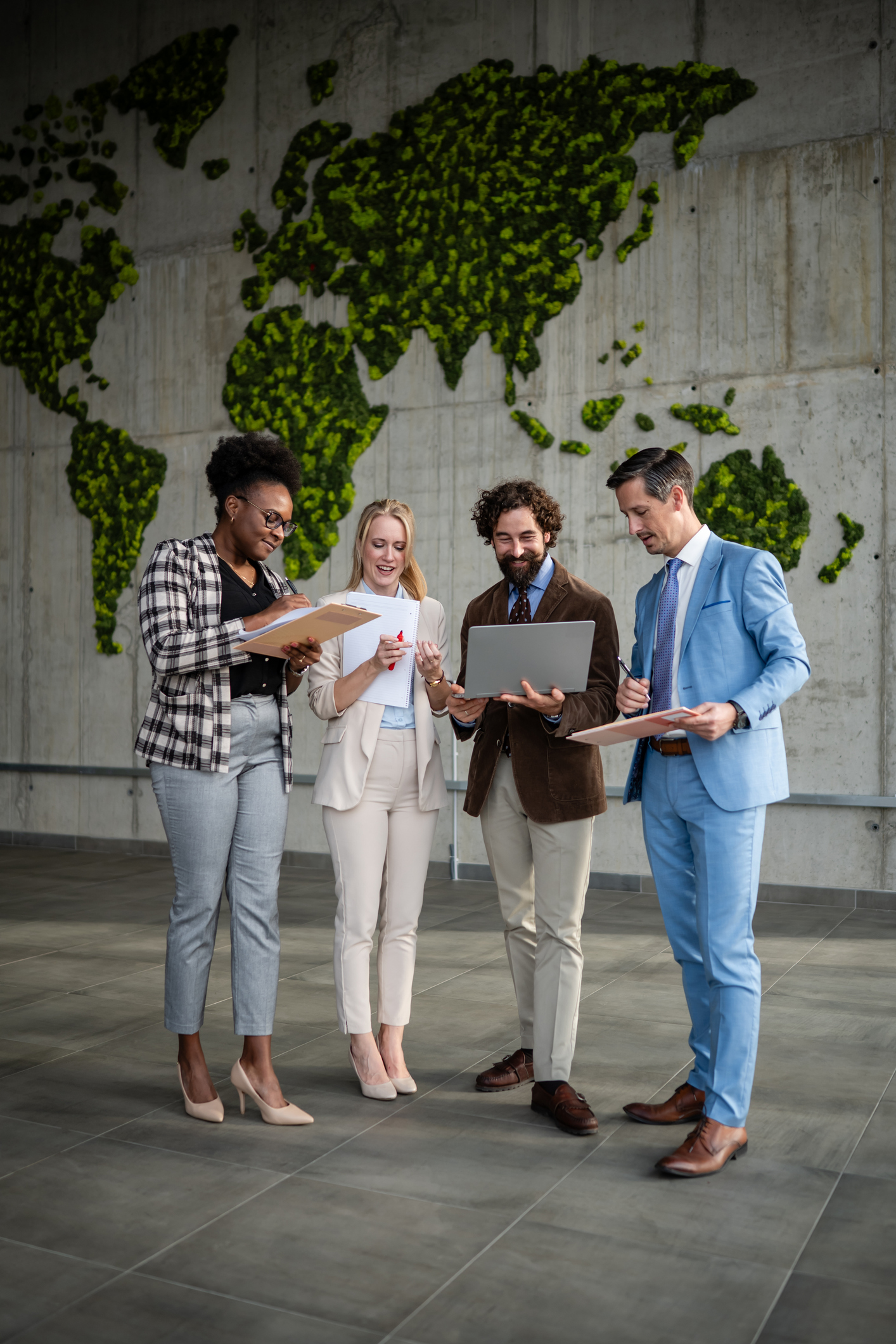 Diverse business professionals discussing work, using a laptop and documents, standing in front of a moss world map wall